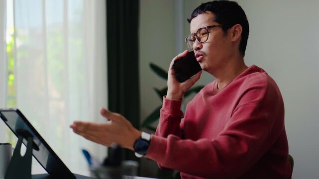 Asian man talking on a smartphone at home, representing everyday communication, modern lifestyle, remote work, and personal conversations indoors.