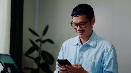 Asian Man Using Smartphone while Working at Desk in Home Office.