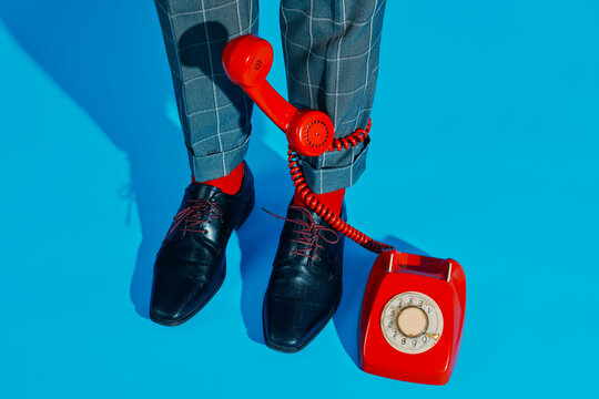 Man legs in plaid trousers with red rotary phone on blue background