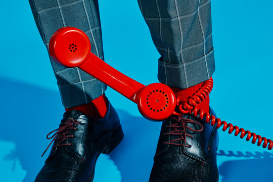 Red telephone handset near shoes with checkered trousers on blue floor