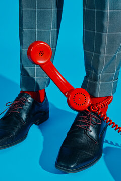 Retro red telephone near man's shoes on vibrant blue background