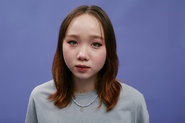 Portrait of a young woman looking at the camera with a serious expression against a blue background