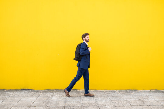 Businessman walking with backpack against yellow wall