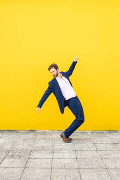 Businessman posing dynamically against yellow wall outdoors