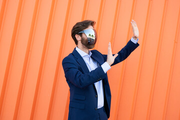 Businessman using VR AR glasses gesturing outdoors against orange wall