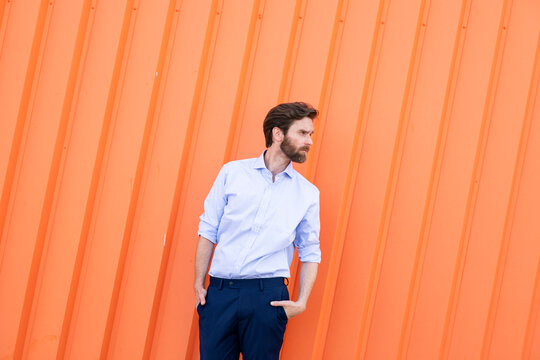 Confident businessman standing with hand in pocket against orange wall