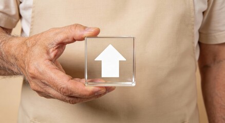 Hands holding glass cube with upward arrow against beige apron ,Active aging Finance concept.