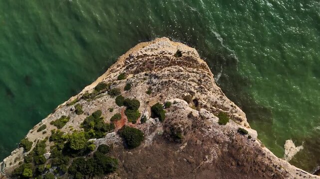 Overhead Aerial View of Alfanzina Lighthouse on Sandstone Cliffs and Sea Caves in Algarve Portugal