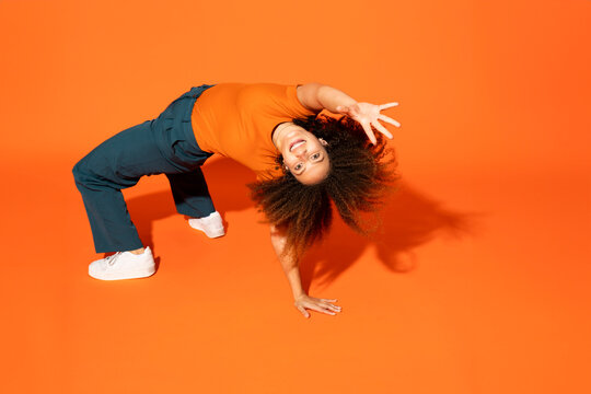 Cheerful woman bending over back in front of orange background