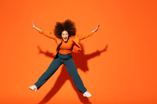 Playful young woman jumping in front of orange background