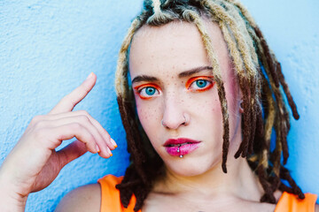 Portrait of woman with dreadlocks piercings and vibrant makeup looking at camera
