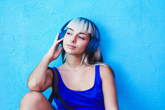 Woman in blue tank top with headphones listening to music by blue wall