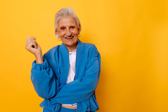 Joyful senior woman in blue jacket smiling against yellow background