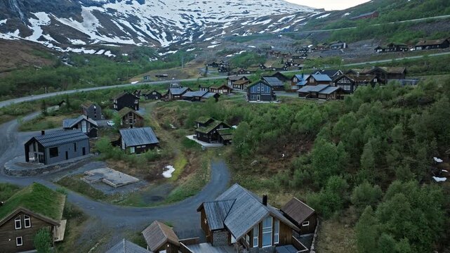Aerial view of mountain houses at R&oslash;ldal Skisenter in Norway. Drone footage showing alpine houses, winding roads, and green hills with snow patches during a calm summer evening.