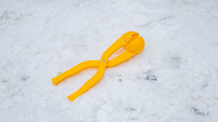 Yellow plastic snowball maker tool resting on a blanket of white snow outdoors. Winter weather toy...