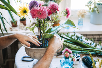 Hands arrange pink and purple aster flowers into stone urn using floral wire mesh. Flower therapy, horticultural therapy, creative wellness, botanical art.