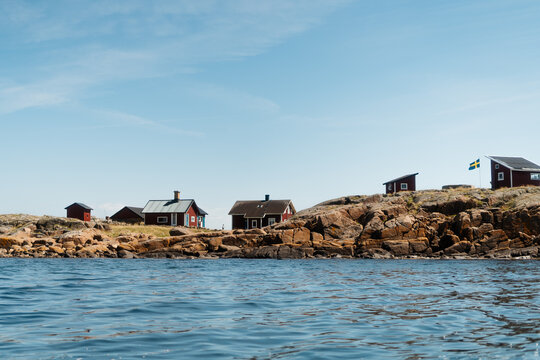 Traditional red wooden cottages on a rocky islet in Varberg archipelago, seen from the water, Sweden