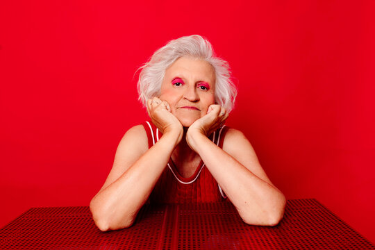 Woman with white hair and pink eyeshadow smiling against a red background