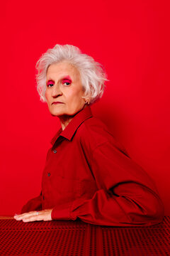 Stylish woman in red shirt with white hair and bold makeup against a red background