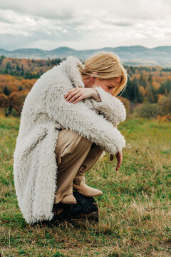 Stylish person in white fleece jacket sitting outdoors in autumn mountains