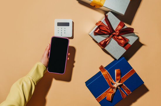 Contactless payment with smartphone and gift boxes on beige background