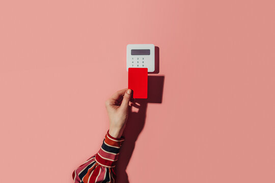 Contactless payment with red card on payment terminal against pink background