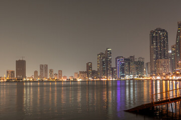 Fototapeta premium Sharjah, UAE,10.10.2025. City skyline at night with water reflections and bright lights in the urban area.