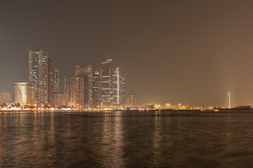 Fototapeta premium Sharjah, UAE,10.10.2025. City skyline at night with water reflections and bright lights in the urban area.