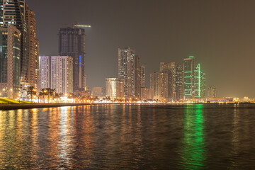 Obraz premium Sharjah, UAE,10.10.2025. City skyline at night with water reflections and bright lights in the urban area.