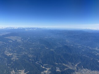 飛行機の窓から撮影した上空の風景 眼下に広がる雲と地上の山々のコントラストが美しい空撮素材 旅の始まりや移動のワクワク感を感じさせる航空写真 広い空と大地の繋がりを表現したダイナミックな構図