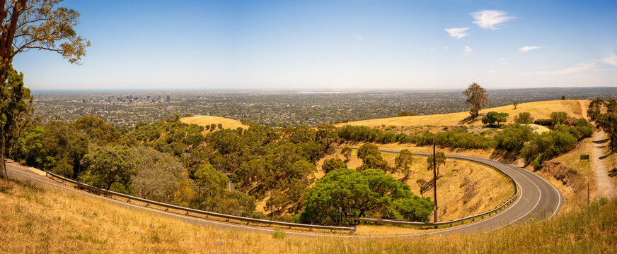 Scenic view of winding road up to hill, Mount Osmond, against blue sky with panoramic city view in the background, Adelaide, South Australia, Australia