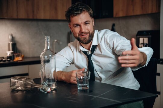 Smiling man in a white shirt and tie gestures while sitting at a kitchen table with a glass and a bottle, conveying a relaxed atmosphere around alcohol consumption - Powered by Adobe