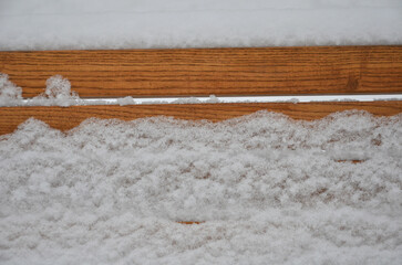 Orange-brown snow covered board of wooden bench. Closeup outdoors photo. Winter environment.	