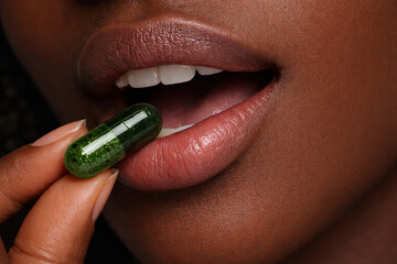 Woman taking green herbal capsule supplement close up