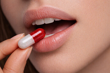 Woman taking red and white capsule supplement close up
