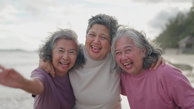 Asian cheerful elderly best friends enjoying a summer holiday together on a beautiful beach by the sea.