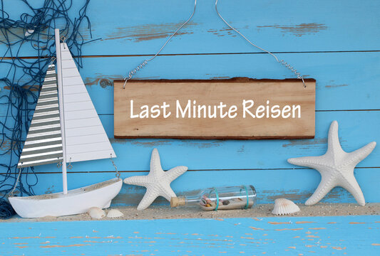 Last Minute Reisen auf ein Schild geschrieben mit maritimer Dekoration, Muscheln, Sand und Seestern.