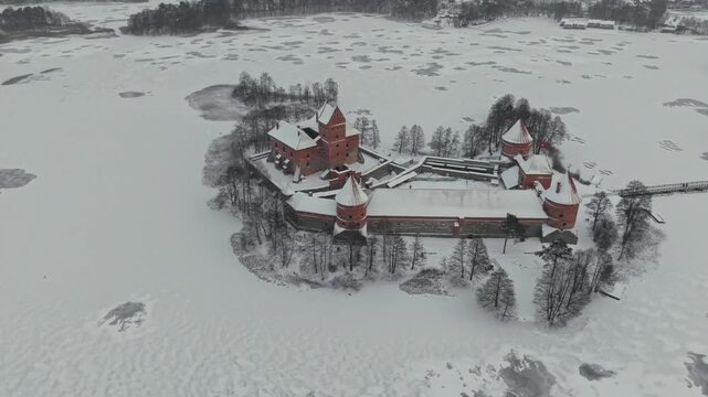 Aerial view of Trakai Castle on a small island in Lake Galve, covered with snow, creating a striking contrast against the icy, winter landscape, Trakai, Lithuania.