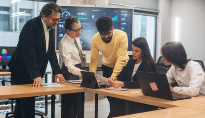 Diverse team of professionals collaborating on a project in a modern office, analyzing data on a tablet and discussing strategies for success