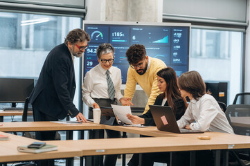 Group of diverse business professionals collaborating on project in modern office, analyzing data on screen and discussing strategies for success and innovation