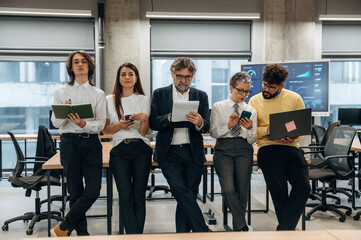 Group of diverse business professionals collaborating in modern office space, engaged with digital devices, showcasing teamwork and innovation in a corporate environment