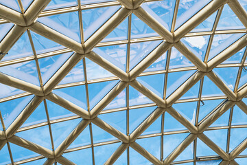 Geometric glass and metal ceiling structure creating triangular grid against the blue sky