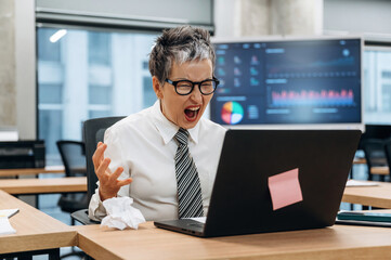 Naklejka premium Businesswoman expressing frustration while working on laptop in modern office environment, showcasing the challenges of remote work and digital communication