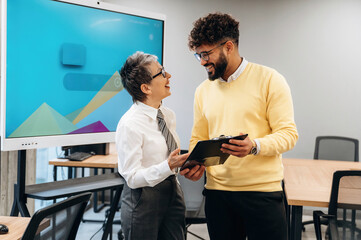 Business professionals engaging in a collaborative discussion in a modern office environment with digital screen and wooden tables, showcasing teamwork and innovation