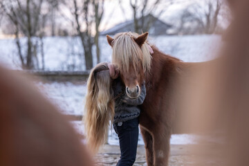 Young woman hugging an Icelandic horse on a winter paddock, expressing calmness, affection, trust and emotional connection