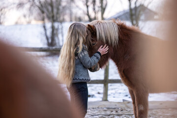 Young woman hugging an Icelandic horse on a winter paddock, expressing calmness, affection, trust and emotional connection