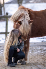 Young woman hugging an Icelandic horse on a winter paddock, expressing calmness, affection, trust and emotional connection