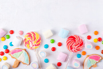 Flat lay with sweets assortment on white.  Lollipops, marshmallow, umbrella cookie and candy drops. Copy space