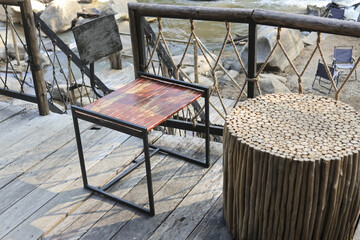 Outdoor wooden terrace balcony featuring metal table and round stick stool next to rope railing...