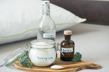 Baking soda, vinegar, and borax, salt are placed on a wooden tray. The scene shows a tidy indoor space with natural light. Sustainable, non-toxic home care solution for fresh and hygienic bedding.